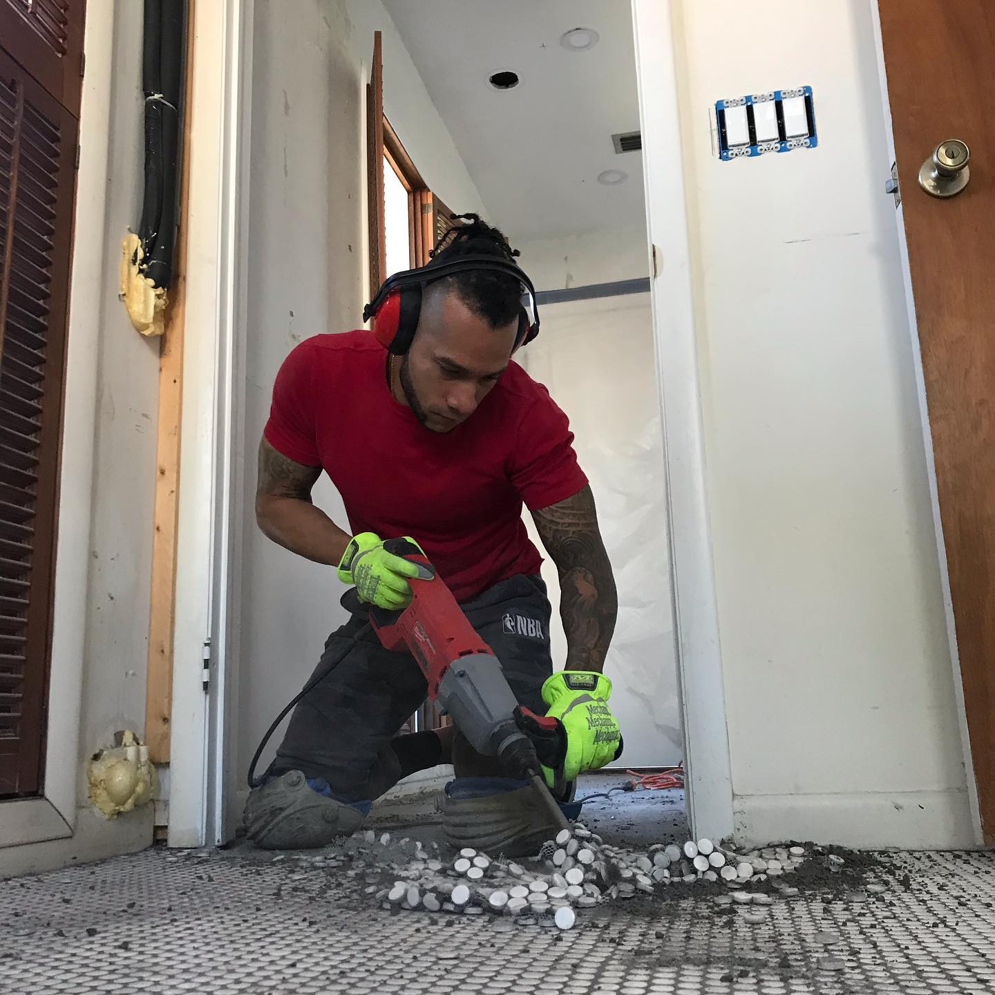 Installer using a demolition hammer to remove old mosaic floor tile in a doorway